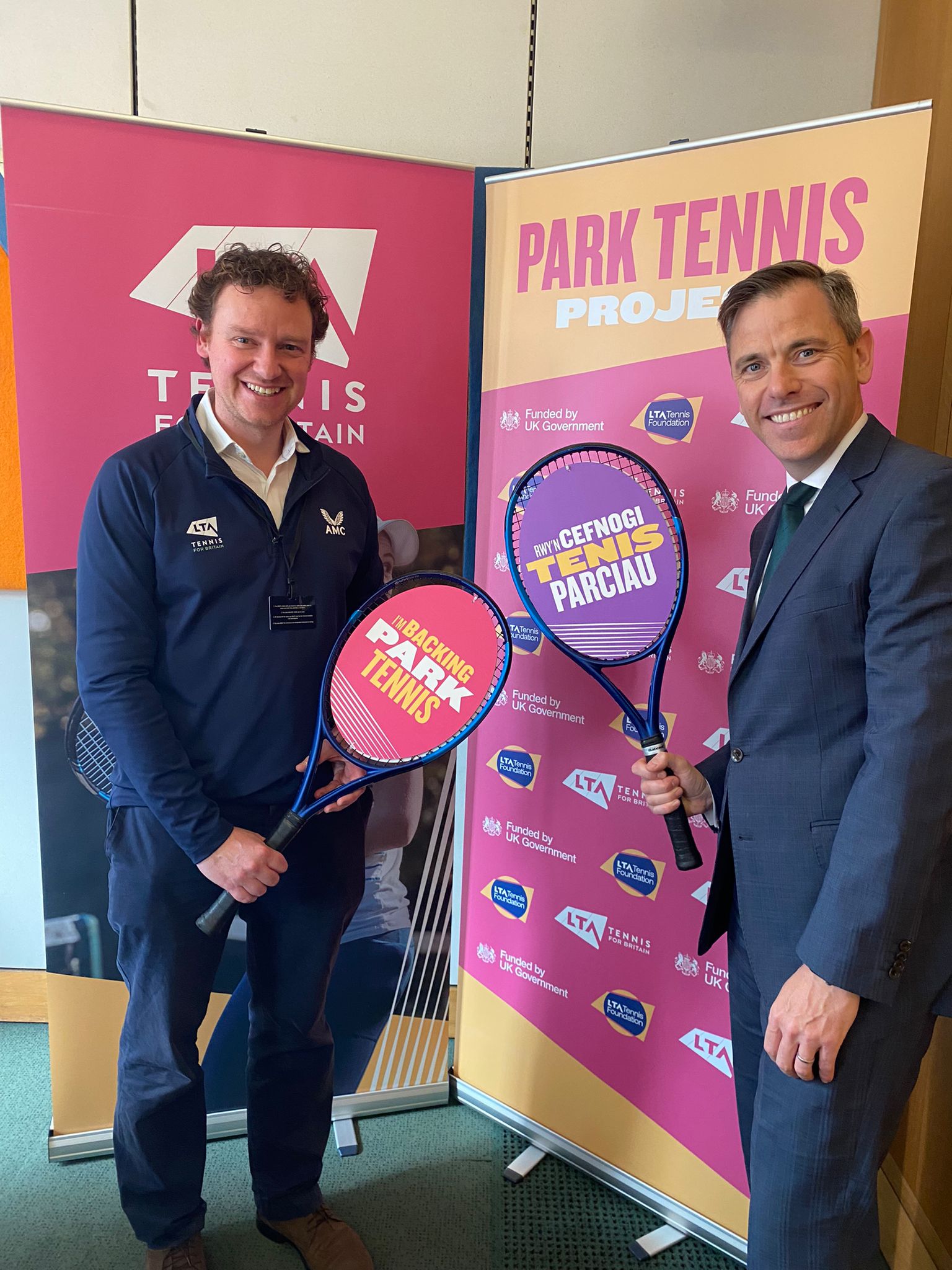 Two Men, including Chris Evans MP, holding tennis rackets that read "I'm backing park tennis"